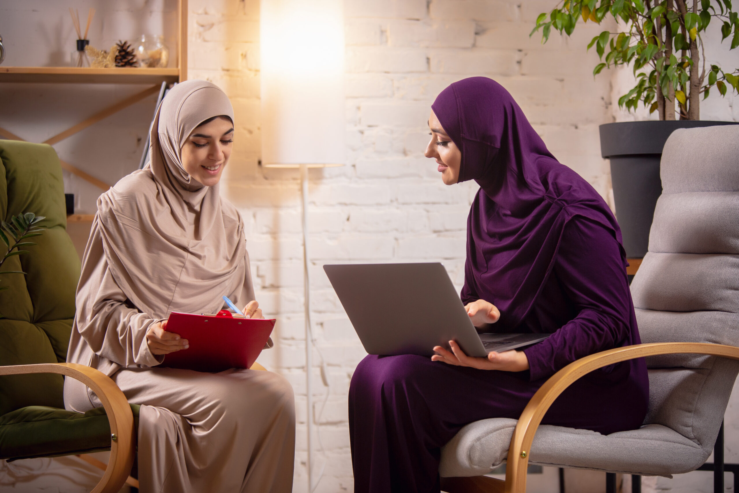 Happy two muslim women at home during lesson, studying near computer, online education